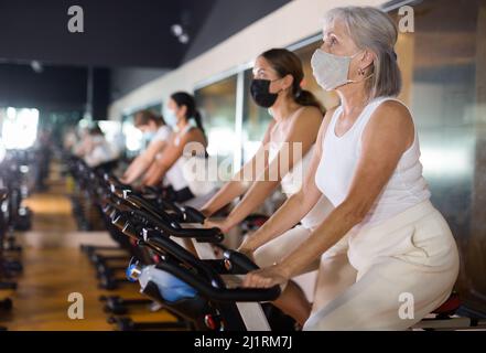 Femme adulte sous masque avec vélo de fitness dans la salle de gym Banque D'Images