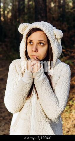 Une jeune femme dans un sweat à capuche blanc molletonné se rétrécit du froid dans la forêt Banque D'Images