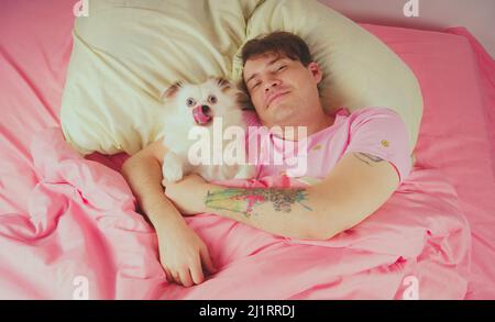 Bel homme allongé avec un chien au lit. Jeune homme dans un lit sous un tapis avec son chien dans une étreinte Banque D'Images