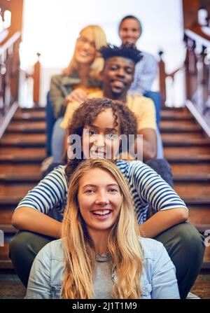 Tout sur le chemin d'un avenir meilleur. Portrait d'un groupe de divers étudiants d'université assis dans une rangée sur l'escalier sur le campus. Banque D'Images