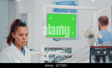 Gros plan du dentiste regardant le moniteur avec écran vert pour l'examen des dents dans le cabinet dentaire. Spécialiste de la dentisterie utilisant la clé chromique avec modèle de maquette et arrière-plan isolé Banque D'Images