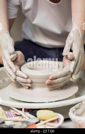 Une femme aux cheveux rouges, au papier blanc et aux jeans, dans un atelier de poterie, travaillant derrière une roue de potier Banque D'Images