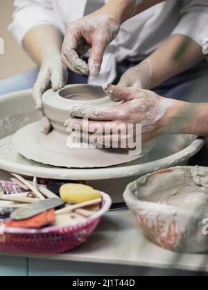 Mains de gros plan, hommes et femmes, une date dans un atelier de poterie, travaillant ensemble sur une roue de potier Banque D'Images