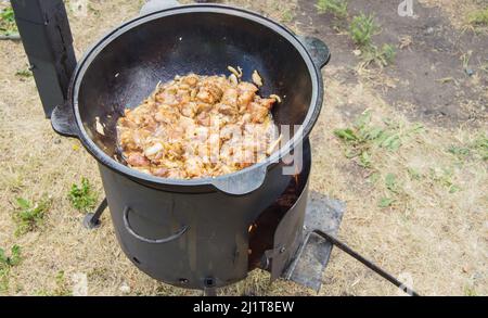 Cuisson de la viande frite dans une grande poêle avec une cheminée, dîner en famille à l'extérieur, gros plan. Banque D'Images