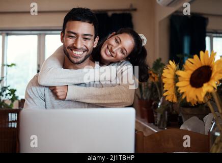 J'espère que je ne suis pas dérangeant Photo d'un homme utilisant son ordinateur portable alors que sa petite amie l'embrasse de derrière. Banque D'Images