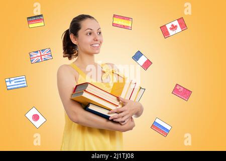 Journée mondiale du livre. Une jeune étudiante souriante en robe jaune tient une pile de livres. Fond jaune avec drapeaux de différents pays. Le conc Banque D'Images