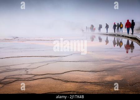 Wyoming, Etats-Unis - 1 octobre 2019 : scène brumeuse de touristes marchant sur une promenade en bois à l'intérieur de la surface humide orange de Grand Prismatic Spring, le plus famo Banque D'Images