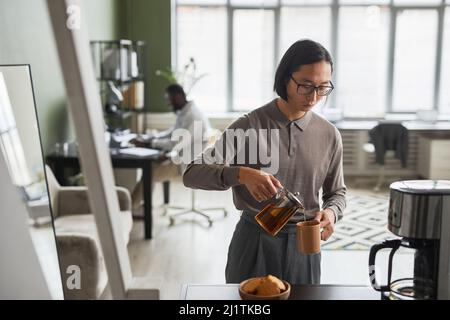 Mini portrait de la taille vers le haut du jeune homme asiatique faisant du café au bureau et portant gris, espace de copie Banque D'Images