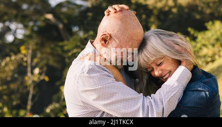 Couple mature se touchant la tête en se tenant debout à l'extérieur. Couple senior heureux partageant un moment romantique au soleil d'été. Couple de personnes âgées e Banque D'Images