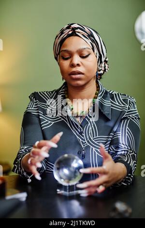 Portrait vertical de la fortune ethnique qui regarde dans la boule de cristal à la seance spirituelle dans le magasin Banque D'Images