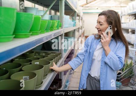 Belle femme dans le centre de jardin choisit des pots en céramique pour transplanter des plantes d'intérieur à la maison.Jardinage, plantation et concept de shopping. Banque D'Images