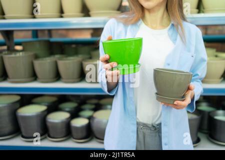 Belle femme dans le centre de jardin choisit des pots en céramique pour transplanter des plantes d'intérieur à la maison.Jardinage, plantation et concept de shopping. Banque D'Images