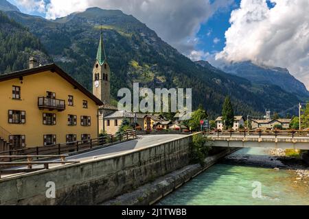 Pont sur la rivière de montagne le long des maisons et de la vieille église en arrière-plan dans la petite ville de Gressoney-Saint-Jean dans la vallée d'Aoste, Italie. Banque D'Images