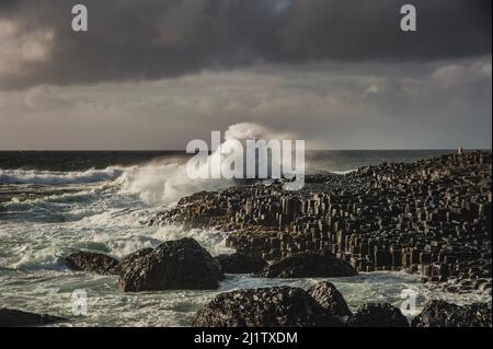 Les vagues de l'océan se brisent sur des rochers hexagonaux au pont-jetée du géant, un jour trouble. La vague de mer qui frappe une falaise transmet un fort impact ou un concept de gros effet Banque D'Images