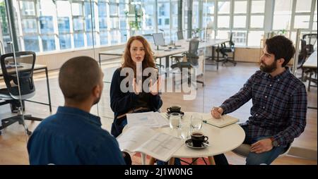 Une jeune femme d'affaires parle avec deux collègues de sexe masculin au cours d'une réunion Banque D'Images