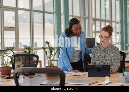 Deux femmes d'affaires diverses travaillant sur une tablette à un bureau Banque D'Images