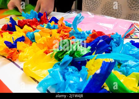 Un enfant décorant une affiche avec des morceaux de papier de soie coloré collés vers le bas. Banque D'Images