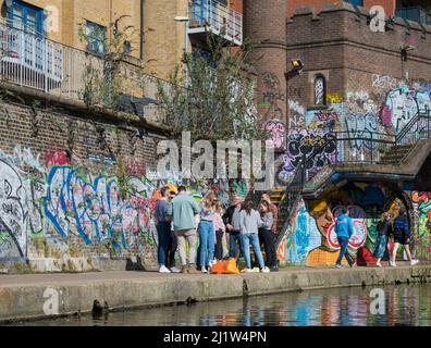 Groupe de personnes en conversation sur le chemin de halage du canal de Regents. Des graffitis colorés couvrent les murs d'arrière-plan. Londres, Angleterre, Royaume-Uni. Banque D'Images