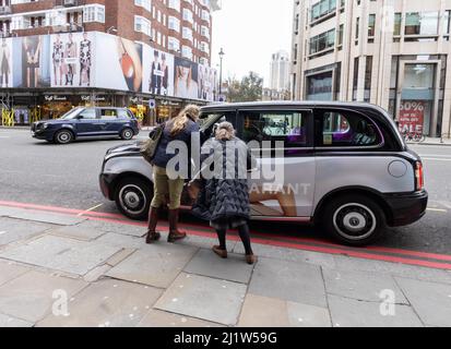 Taxi de Londres; deux femmes qui reçoivent un taxi noir de londres, Knightsbridge, Londres SW1, Londres UK Banque D'Images