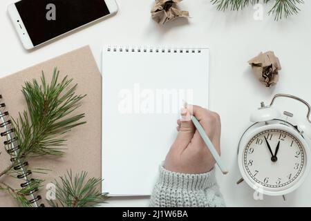 La main de femme écrit dans un cahier vide. Résolutions, plan, objectifs, liste de contrôle, concept d'idée. Flat lay, espace de copie. Noël, nouvel an. Page blanche Banque D'Images