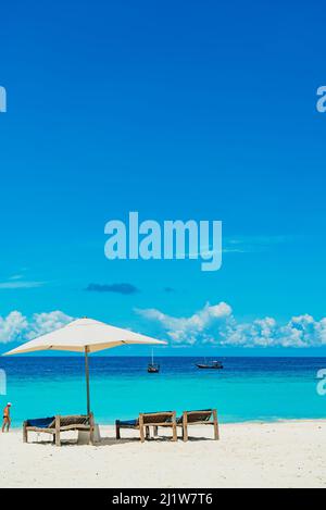 Chaises longues en bois sur une plage de sable en face de l'océan avec des bateaux, Zanzibar Tanzanie Banque D'Images