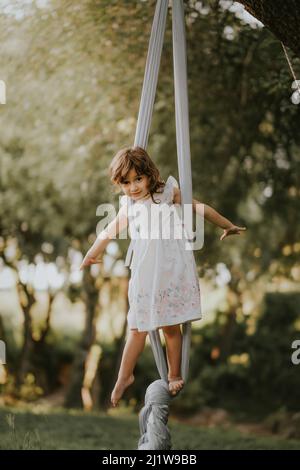 Fille pieds nus en robe teetering sur balançoire dans la campagne herbeuse sur fond flou Banque D'Images