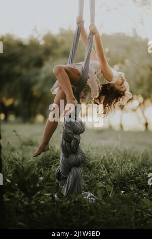 Vue latérale de la fille pieds nus dans la robe teetering sur balançoire dans la campagne herbeuse sur fond flou Banque D'Images