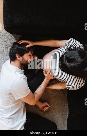 Vue de dessus de doux amoureux mari embrassant le ventre de la femme enceinte tout en se relaxant à la maison Banque D'Images