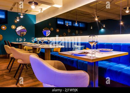Rangée de tables avec assiettes et couverts près des verres dans le restaurant branché avec fauteuils confortables et canapé en velours sous les lampes suspendues au plafond Banque D'Images