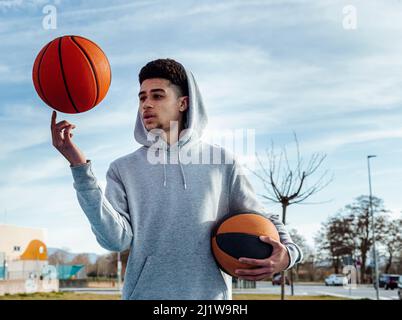 Le sportif hispanique fait tourner le ballon sur le doigt tout en jouant au basket-ball contre le ciel bleu le jour de l'été Banque D'Images