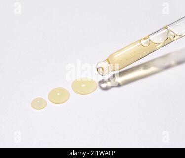 Pipette en verre de dessus avec acide hyaluronique jaune pour le soin de la peau sur fond blanc avec liquide renversé Banque D'Images