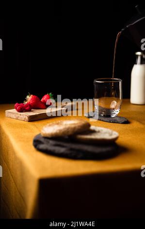 Café frais et parfumé versé dans un verre sur une assiette d'ardoise du pot de moka pour le petit déjeuner avec bagel et framboises avec fraises Banque D'Images