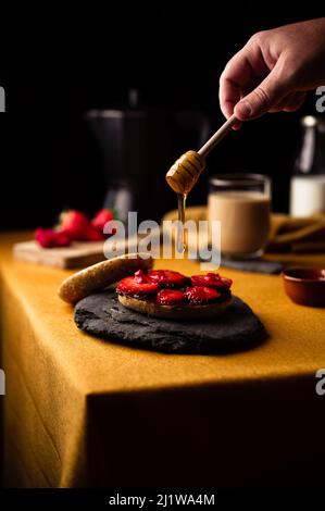 Pour le petit-déjeuner, la personne anonyme doit se maculer le miel sur le bagel avec des fraises fraîches et de la pâte de chocolat avec du café frais provenant du pot de moka Banque D'Images