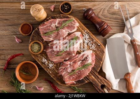 trois steaks de porc de ferme sur une table de cuisson rustique en bois avec des ingrédients. vue sur le dessus. table rustique Banque D'Images