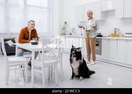 Couple souriant regardant la frontière chien collie dans la cuisine Banque D'Images