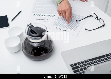 Vue courte d'une femme âgée montrant le contrat près des gadgets et du café dans la cuisine Banque D'Images