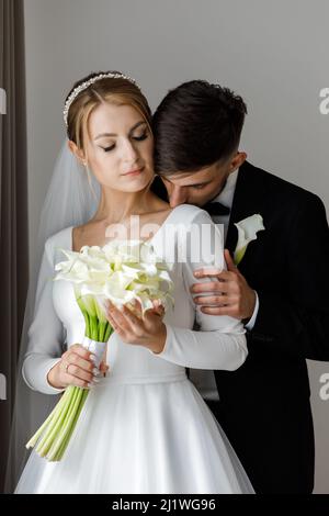 Une jolie mariée habille une mariée dans une robe de mariée. Les jeunes mariés s'embrassent dans la chambre et passent du temps ensemble Banque D'Images