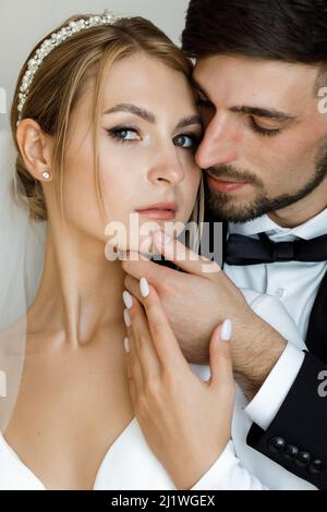 Une jolie mariée habille une mariée dans une robe de mariée. Les jeunes mariés s'embrassent dans la chambre et passent du temps ensemble Banque D'Images