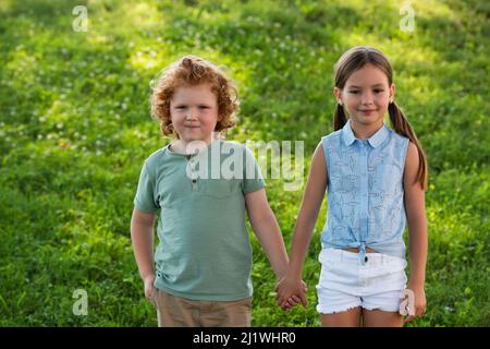 frère et sœur heureux tenant les mains et regardant l'appareil photo à l'extérieur Banque D'Images