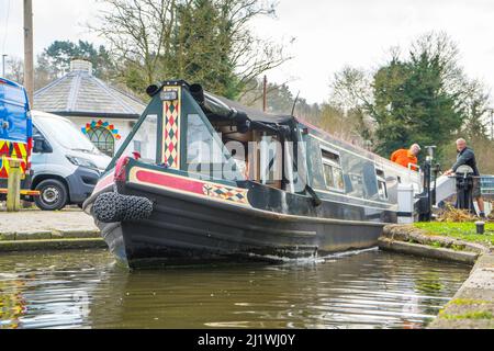 Gros plan sur le bateau à narrowboat en passant par l'écluse ouverte sur le canal du Royaume-Uni avec un homme à l'arrière du bateau. Banque D'Images