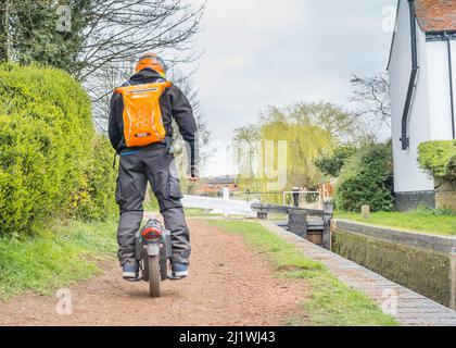 Vue arrière d'un homme isolé qui s'équilibre bien, qui traverse un monocycle électrique le long d'un chemin de halage du canal britannique. Banque D'Images