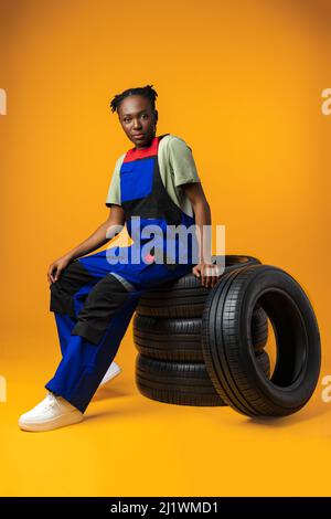 Portrait d'une femme mécanique noire souriante posant avec de nouveaux pneus de voiture en studio Banque D'Images