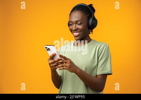 Bonne jeune Afro-américaine femme écoutant de la musique dans des écouteurs sur fond jaune Banque D'Images