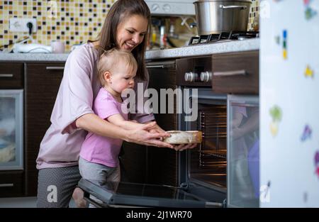 Petite petite fille drôle mignon aidant la mère à préparer le gâteau de tarte dans la cuisine, la cuisson de biscuits maison ensemble, heureux temps de famille. Banque D'Images