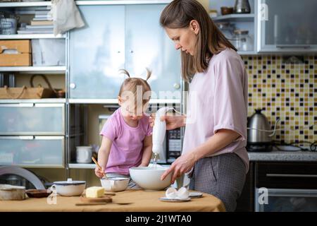 Petite petite fille drôle mignon aidant la mère à préparer le gâteau de tarte dans la cuisine, la cuisson de biscuits maison ensemble, heureux temps de famille. Banque D'Images