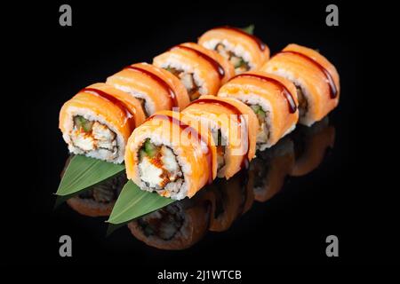Délicieux sushi traditionnel frais sur fond noir avec reflet. Sushi roulent avec du riz, du nori, du fromage à la crème, du tobiko caviar, de l'avocat. Su Banque D'Images