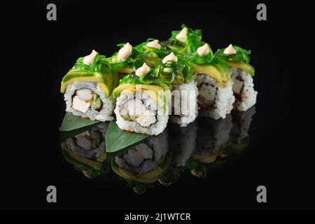 Délicieux sushi traditionnel frais sur fond noir avec reflet. Sushi roulent avec du riz, du nori, du fromage à la crème, du tobiko caviar, de l'avocat. Su Banque D'Images