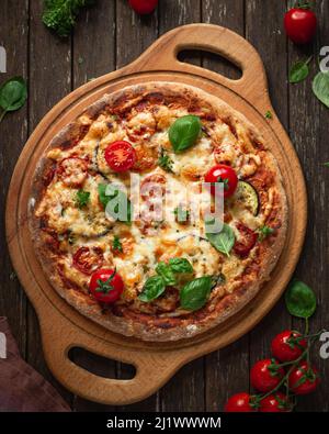 Pizza végétarienne pleine fleur avec aubergines, tomates cerises et feuilles de basilic sur fond de bois brun foncé, vue du dessus Banque D'Images