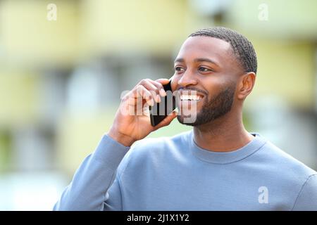 Un homme heureux à la peau noire parle sur un téléphone portable à l'extérieur de la rue Banque D'Images