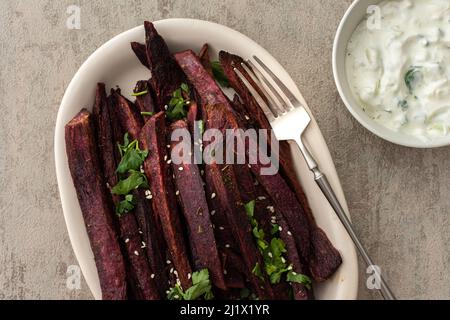 Quartiers de patates douces au four avec épices et persil dans un plat ovale en céramique, sauce avocat avec yaourt et épices Banque D'Images